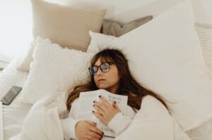 ベッドの上で本を抱えて眠る女性