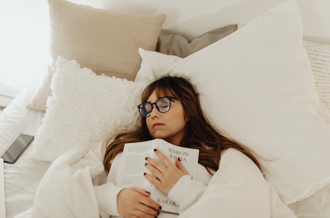 ベッドの上で本を抱えて眠る女性