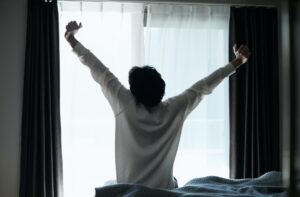 窓に向かって伸びをしている男性の後ろ姿