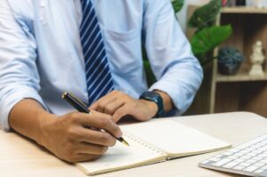 ノートに書き物をしている男性の手元