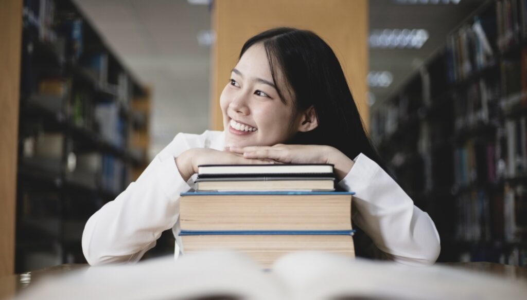 図書館で、積み重ねた本の上に顔を乗せて笑っている女性