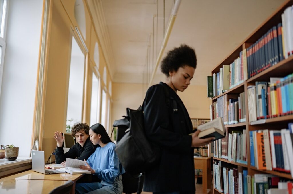 図書館で本棚の前に立ち本を読んでいる学生