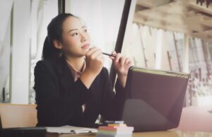 パソコンを開いて上を見ながら考え事をする女性