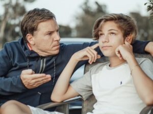 隣で父に何かを言われ、耳を塞いで聞かないようにしている少年