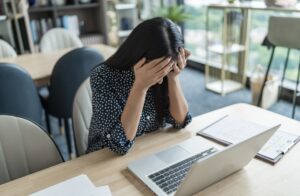 パソコンを見ながら顔に手を当てて悩む女性